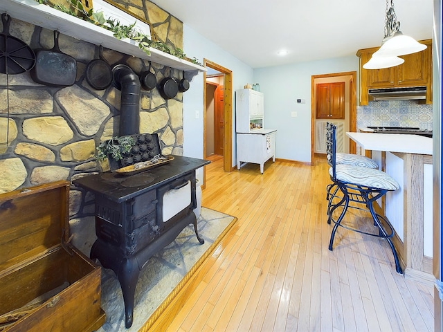 kitchen featuring a wood stove, tasteful backsplash, light hardwood / wood-style flooring, pendant lighting, and a breakfast bar area