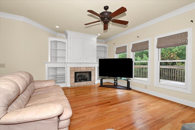 living room with a fireplace, ornamental molding, ceiling fan, and light wood-type flooring