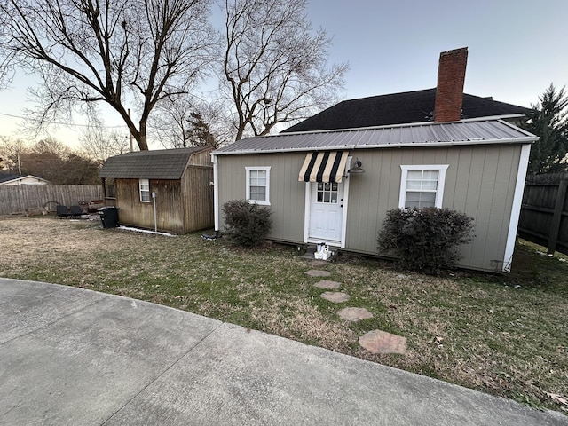 view of front of home featuring an outbuilding, metal roof, a storage shed, fence, and a yard