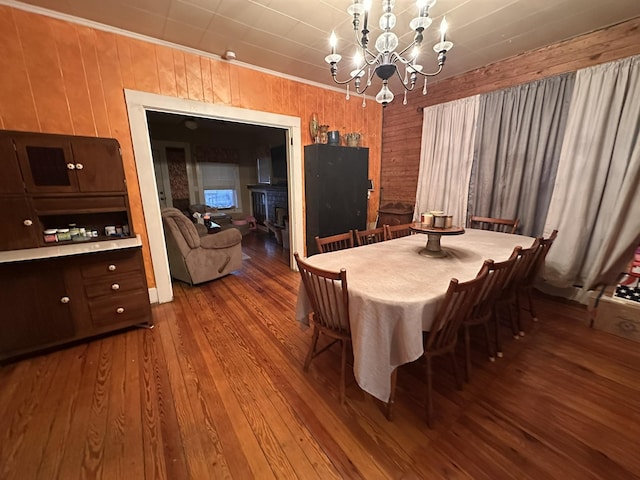 dining room with crown molding, a fireplace, wooden walls, wood finished floors, and a chandelier