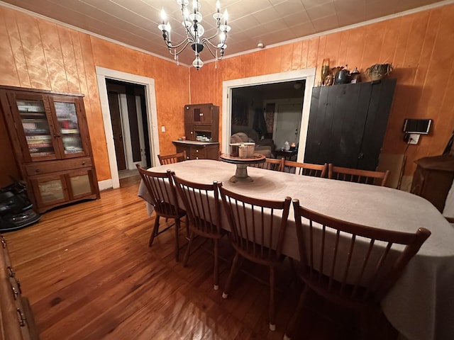 dining area featuring a chandelier, ornamental molding, wood finished floors, and wooden walls