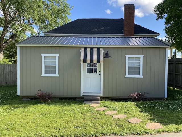 rear view of property with metal roof, a yard, an outdoor structure, and fence