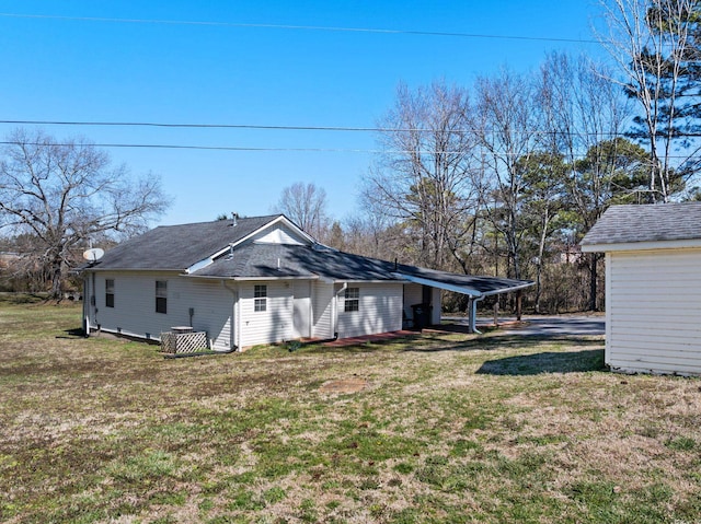 back of house featuring roof with shingles, a carport, and a yard