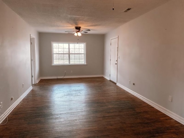 spare room featuring visible vents, a ceiling fan, dark wood finished floors, and baseboards