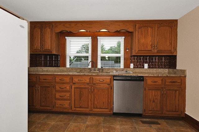  - kitchen featuring stainless steel dishwasher, freestanding refrigerator, brown cabinetry, backsplash, and light stone countertops