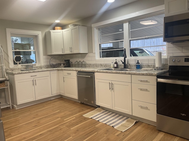 kitchen with sink, stainless steel appliances, light hardwood / wood-style flooring, decorative backsplash, and white cabinets