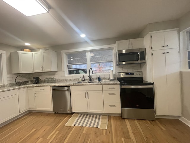 kitchen with appliances with stainless steel finishes, tasteful backsplash, sink, light hardwood / wood-style flooring, and white cabinets