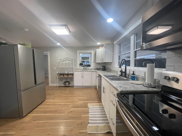 kitchen with appliances with stainless steel finishes, tasteful backsplash, sink, white cabinets, and light hardwood / wood-style floors