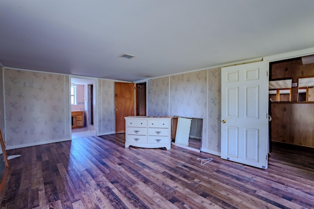 unfurnished bedroom with baseboards, wallpapered walls, wood finished floors, and visible vents