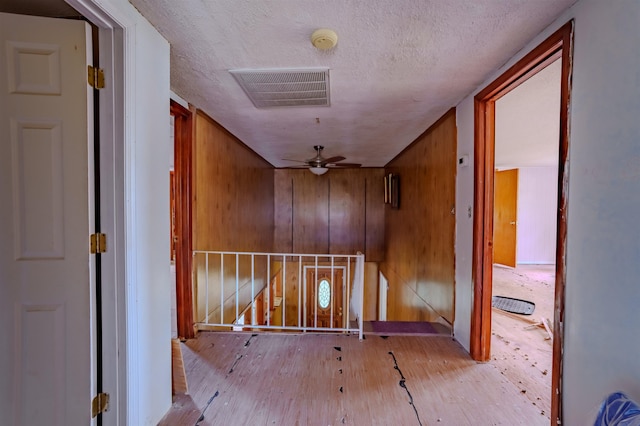 corridor featuring wood walls, visible vents, an upstairs landing, light wood-style flooring, and a textured ceiling