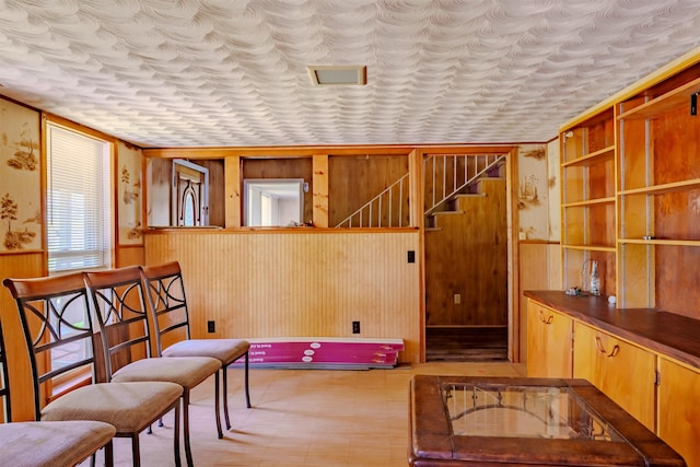 living area featuring a textured ceiling, wood walls, stairs, and wainscoting