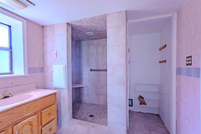full bathroom featuring tile walls, vanity, tiled shower, and visible vents