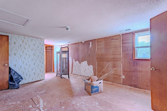 basement featuring wood walls, visible vents, and a textured ceiling