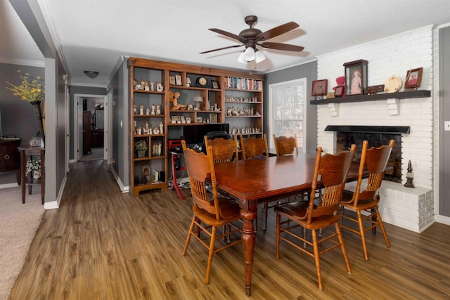 dining area with a brick fireplace, ceiling fan, ornamental molding, a textured ceiling, and wood-type flooring