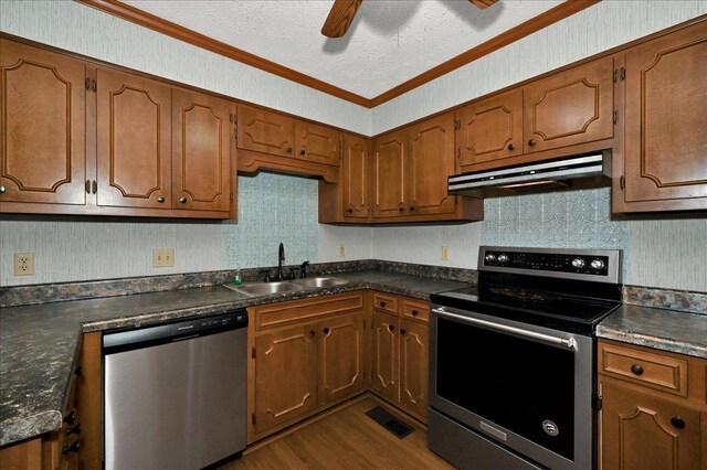  - kitchen featuring appliances with stainless steel finishes, under cabinet range hood, a sink, dark countertops, and ornamental molding
