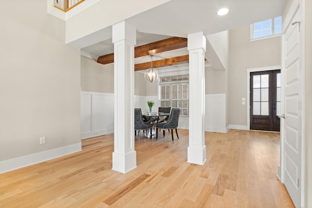 entryway featuring light wood-style flooring, beam ceiling, a wainscoted wall, and decorative columns