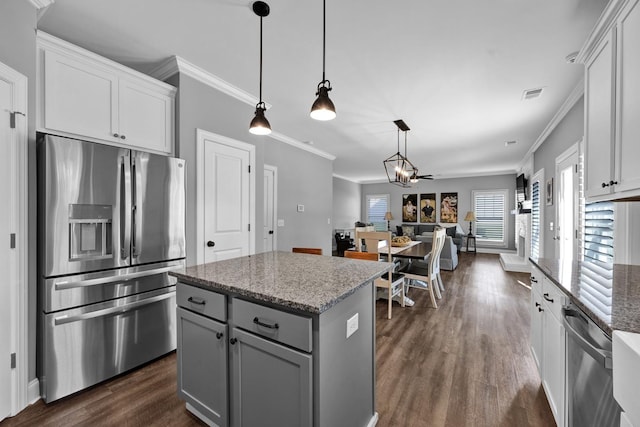 kitchen with light stone countertops, stainless steel appliances, pendant lighting, a center island, and white cabinetry