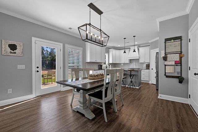 dining space with a notable chandelier, sink, ornamental molding, and dark wood-type flooring