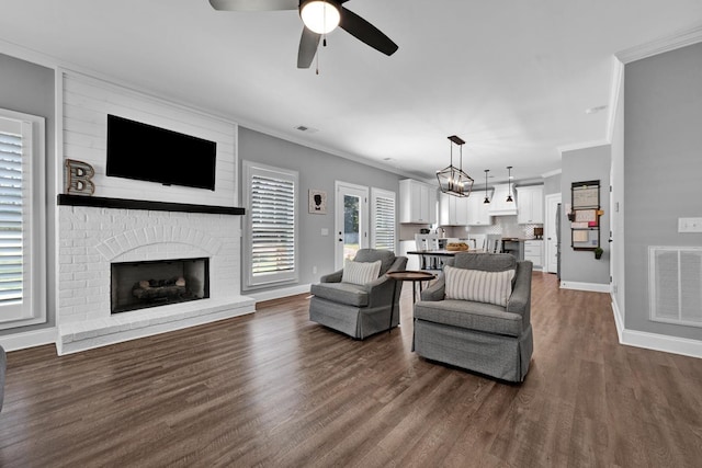 living room with a fireplace, dark wood-type flooring, ceiling fan with notable chandelier, and ornamental molding