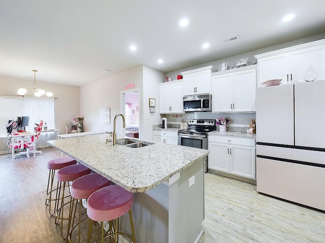 kitchen featuring sink, hanging light fixtures, stainless steel appliances, a center island with sink, and white cabinets