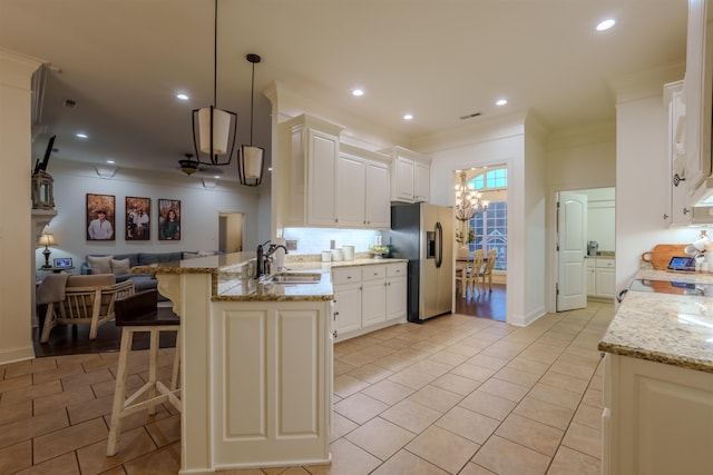 kitchen with sink, kitchen peninsula, stainless steel fridge, pendant lighting, and white cabinets