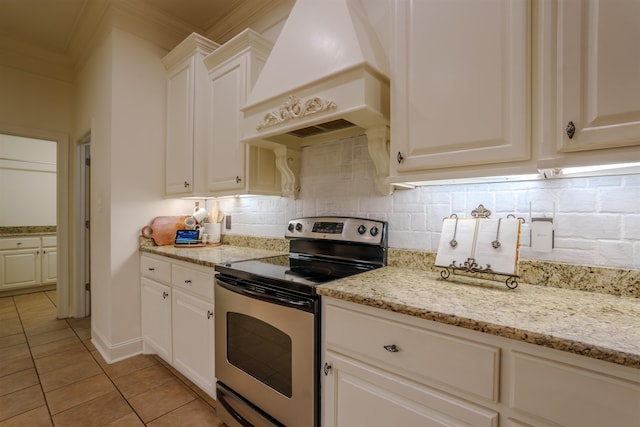 kitchen with light tile patterned floors, light stone counters, stainless steel electric stove, white cabinets, and custom exhaust hood