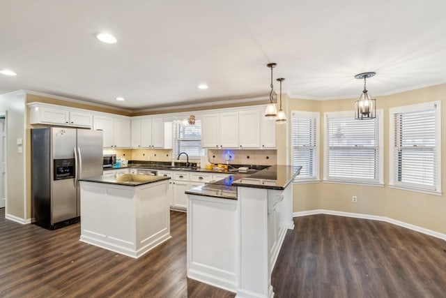 kitchen with a center island, sink, appliances with stainless steel finishes, decorative light fixtures, and white cabinetry