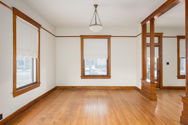unfurnished room with a wealth of natural light, decorative columns, light wood-style flooring, and baseboards