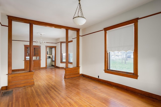 empty room featuring baseboards, a chandelier, and light wood-type flooring