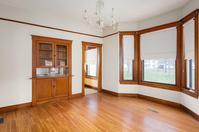 unfurnished room featuring visible vents, a healthy amount of sunlight, light wood-style floors, and a notable chandelier