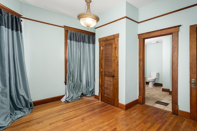 bedroom with baseboards, ensuite bathroom, a closet, and wood-type flooring