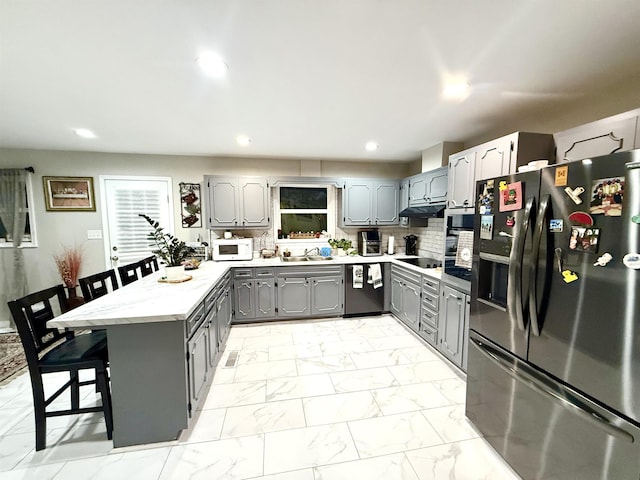 kitchen featuring marble finish floor, gray cabinetry, a peninsula, appliances with stainless steel finishes, and a breakfast bar area