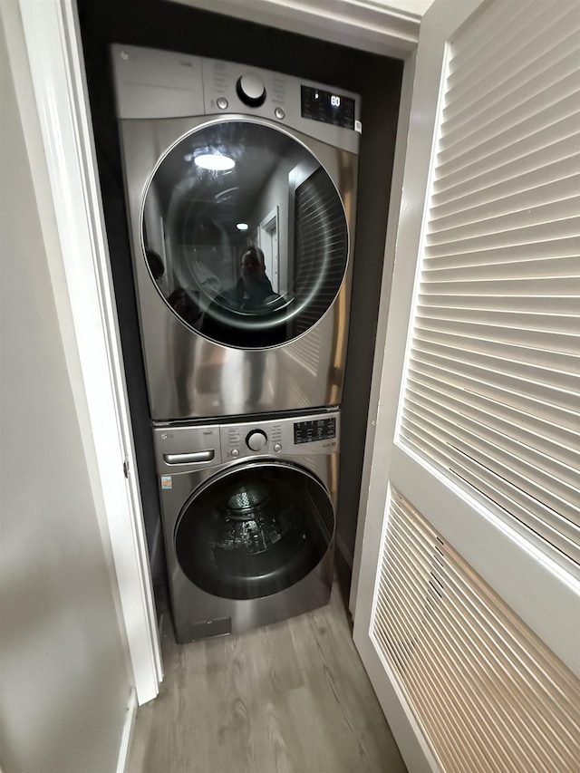 laundry room featuring stacked washer and dryer, wood finished floors, and laundry area