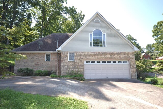 view of side of property featuring driveway, an attached garage, and brick siding