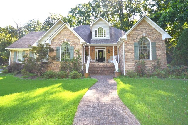 view of front facade featuring brick siding, roof with shingles, a porch, and a front yard