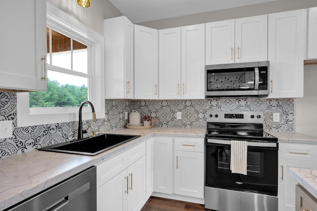  - kitchen featuring appliances with stainless steel finishes, a sink, white cabinetry, and backsplash