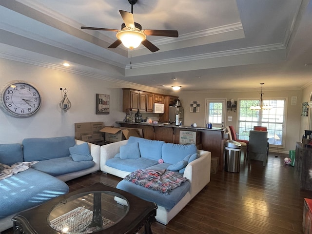 living room with a tray ceiling, crown molding, dark hardwood / wood-style flooring, and ceiling fan with notable chandelier