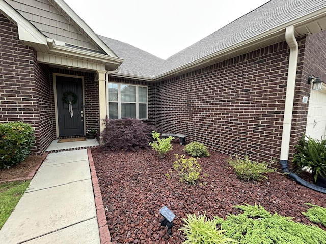  - doorway to property with brick siding, a shingled roof, and a garage