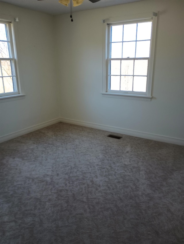unfurnished room with a ceiling fan, visible vents, dark carpet, and baseboards