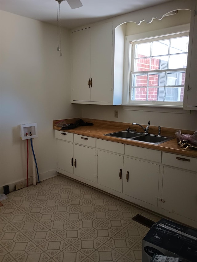 kitchen with arched walkways, white cabinetry, baseboards, and a sink