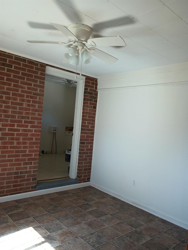empty room featuring brick wall, baseboards, stone finish flooring, and ceiling fan