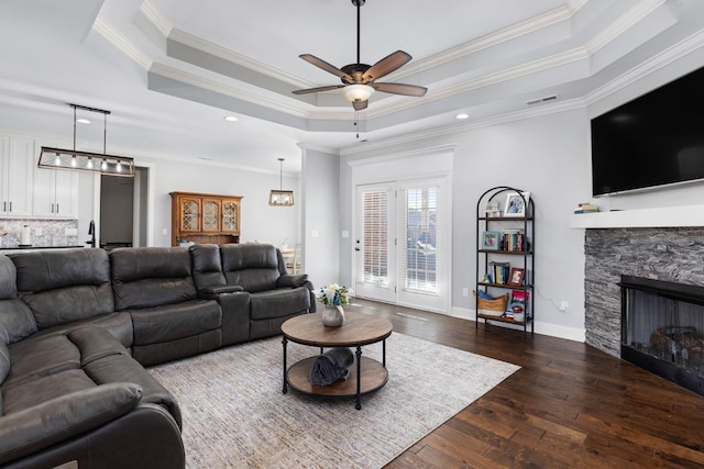 living area with a tray ceiling, visible vents, a ceiling fan, ornamental molding, and wood-type flooring