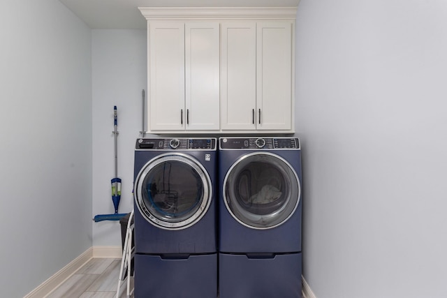 clothes washing area featuring separate washer and dryer, baseboards, and cabinet space