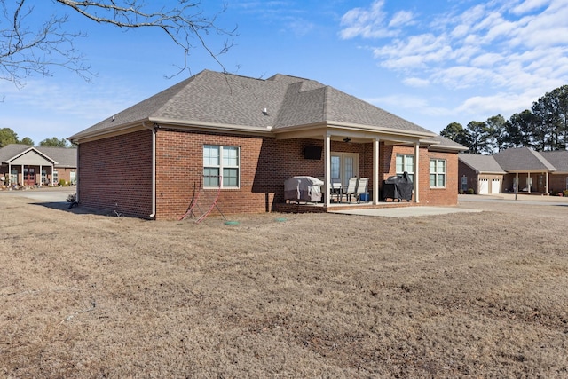 rear view of house with brick siding, roof with shingles, and a patio