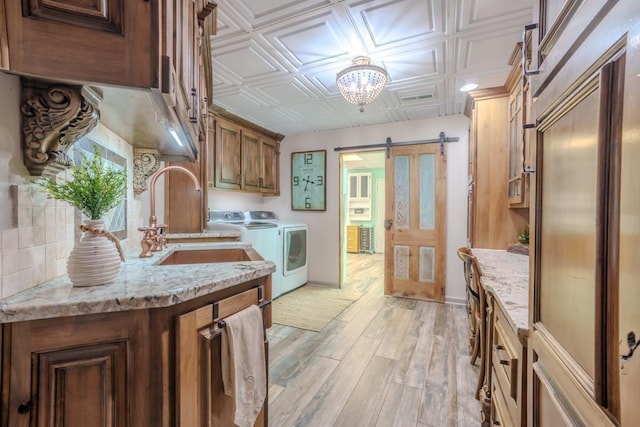  - kitchen featuring washing machine and dryer, a sink, a barn door, light wood-style flooring, and light stone countertops