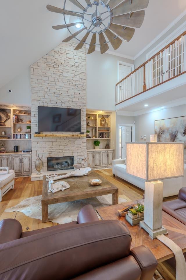  - living room with high vaulted ceiling, a ceiling fan, wood finished floors, ornamental molding, and a stone fireplace
