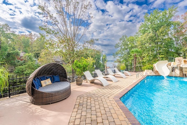  - view of swimming pool with a water slide, a patio area, fence, and view of scattered trees