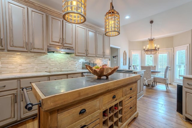  - kitchen with a chandelier, under cabinet range hood, black electric stovetop, backsplash, and pendant lighting