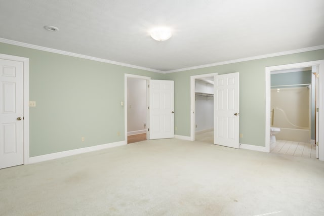 unfurnished bedroom with connected bathroom, a walk in closet, light colored carpet, crown molding, and a closet