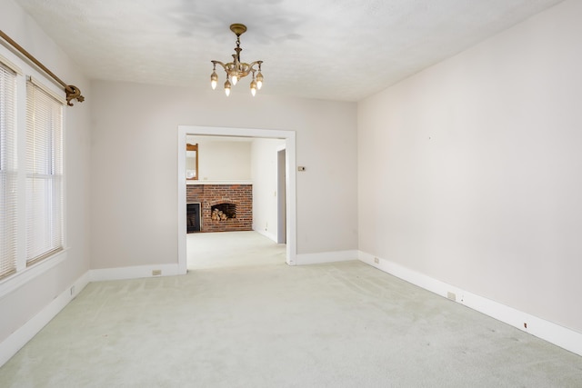 carpeted spare room featuring a brick fireplace and a chandelier